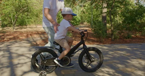 Boy rides bicycle with father support on training wheels Stock Footage 316764348