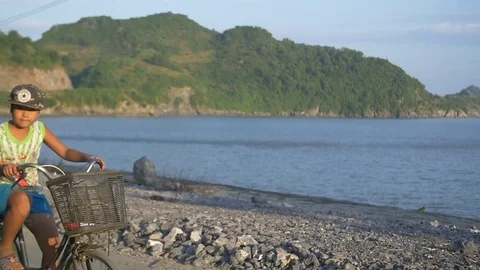 Boy rides bicycle with ocean in background - pan shot Stock Footage 70600872