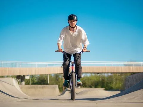 Boy rides on BMX, looking at camera in ramp park 스톡 사진
