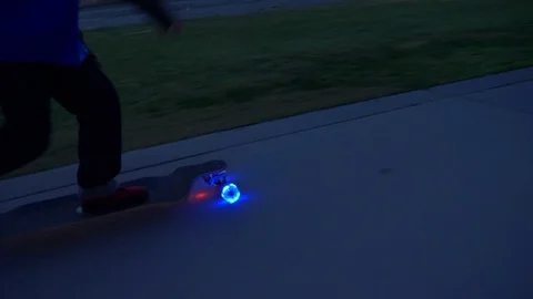 A boy rides a skateboard with led lights wheels in a neighborhood. Stock Footage