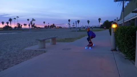 A boy rides a skateboard with led lights wheels in a neighborhood. Stock Footage