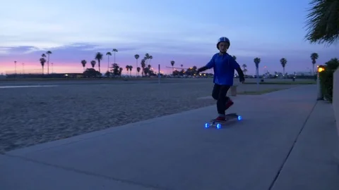 A boy rides a skateboard with led lights wheels in a neighborhood. Stock Footage