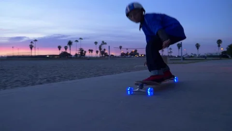 A boy rides a skateboard with led lights wheels in a neighborhood, slow motion. Stock Footage