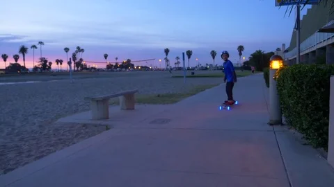 A boy rides a skateboard with led lights wheels in a neighborhood, slow motion. Stock Footage