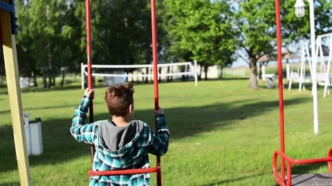 The boy rides a swing on a warm sunny day. Back view bakground Stock Footage 81005643