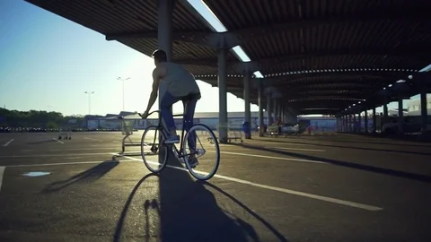 Boy riding bicycle empty car parking circling pillars sunrise slow motion rapid Video stock 78040484