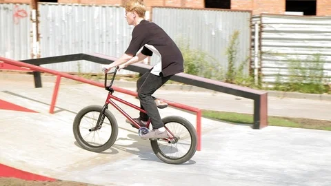 A boy is riding BMX cycling tricks in a skateboard park on a sunny day. Super Stock Footage 92894635