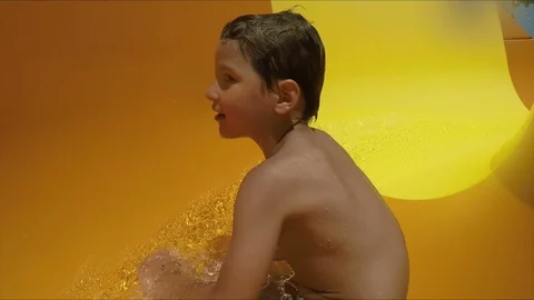 Boy is riding down rotating an orange slide in a water park Stock-Footage 128397438
