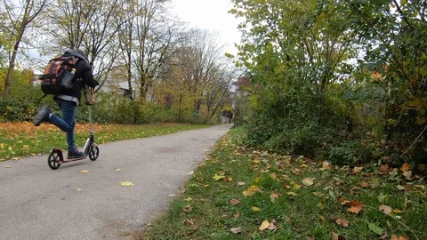 A boy is riding a push scooter along a path through the park on a fall November 스톡 동영상 119856938
