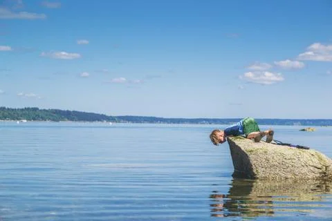 Boy on a rock looking down at his reflection in the sea Stock Photos