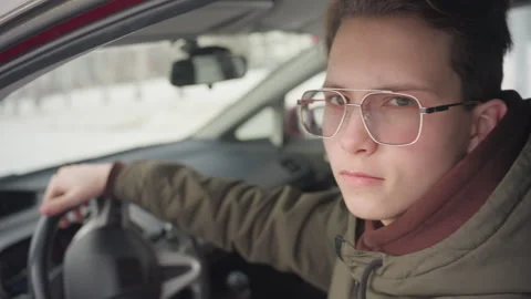 Boy rolling down window inside car holding steering with calm expression Stock Footage 310180298