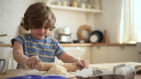 Boy rolling out dough and having fun, sitting at table in apartment kitchen. Stock Footage 158980306