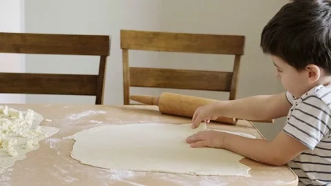 Boy rolling out the dough with a rolling pin on the table in the kitchen helping Video stock 172506257
