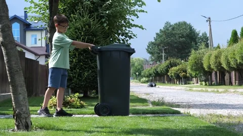Boy rolls out trash can. waste collector garbage removal from a private house. 库存影片 280392511