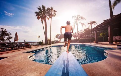 Boy run on diving board jumping to pool at sunset Stock Photos