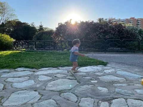 A boy running along a stone path in a park with a sunset in the background. Stock Photos