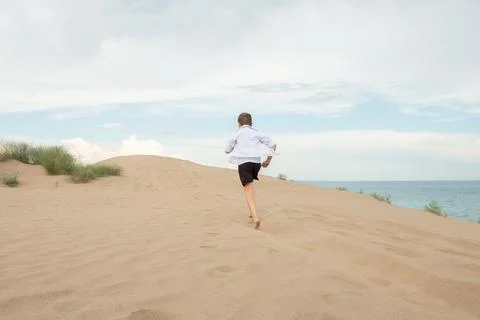 Boy Running Barefoot Up Sandy Dune Near Ocean, Freedom and Adventure Concep.. Stock Photos