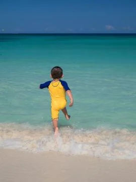Boy running on beach into ocean Stock Photos