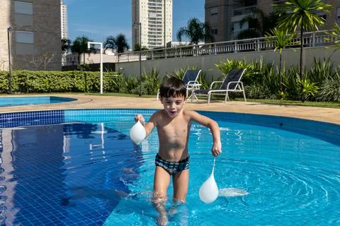 Boy running in the pool with two water balloons. Stock Photos