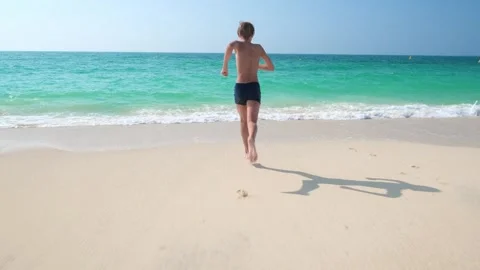Boy running to sea on sandy beach and diving, back view Stock-Footage 292157249