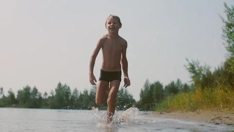Boy running on water making splashes on the shore of a lake on the beach Stock Footage 306219024