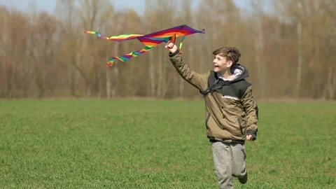 A boy runs across a green field with a kite. front view, slow motion. Видео 196625982