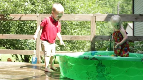 Boy runs around edge of kiddie pool as girl fills it with hose Stock Footage 40028345