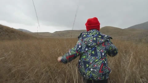 Boy runs on high dry grass among hills on a cloudy day Vídeo Stock 130378178