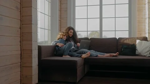 Boy runs to his mom working at the laptop from home and hugs her on a couch Stock Footage 165414010