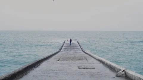Boy runs through a concrete structure in the sea, the waves hit the stone coast Stock Footage 128242984