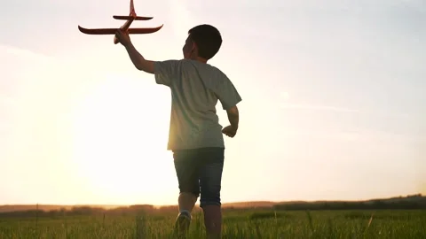 Boy runs with toy plane through grassy field at sunset, silhouette of child Stock Footage 317161622