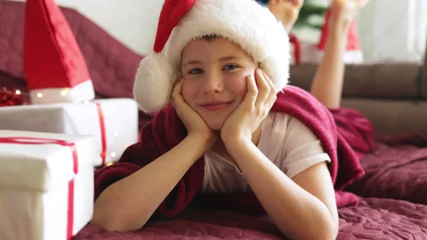 Boy in Santa Claus hat lying on bed and receiving a present in gift box Stock Footage 164712149