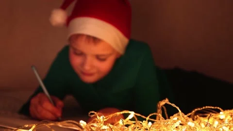 A boy in a Santa Claus hat writes a letter while lying on the bed on a Christmas Stock Footage 165395616