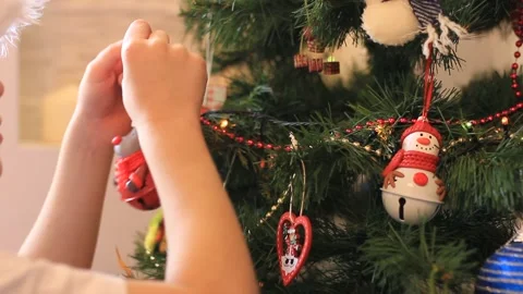 Boy in a Santa hat hangs Christmas toys on the Christmas tree. HD video, 25 FPS Stock Footage 166292386