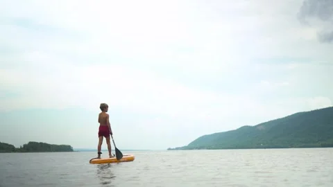 A boy on a sapsurf swims along the river against the background of the river. A Stock Footage 247628102