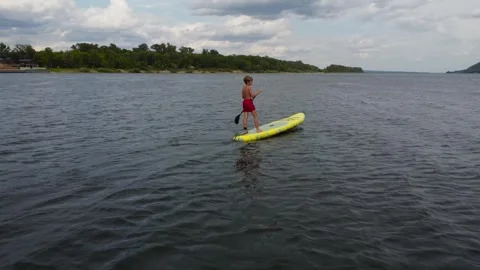 A boy on a sapsurf swims along the river against the background of the river. A Stock Footage 247628439