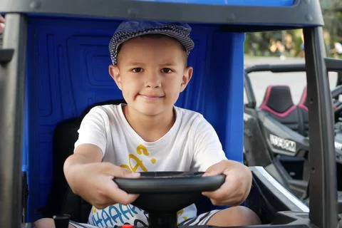 A boy with a satisfied expression on his face sitting in a toy car holding the w Foto stock