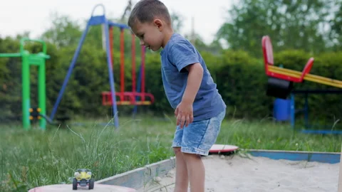 A boy scatters sand while playing in a sandbox on the playground Stock Footage 218877941