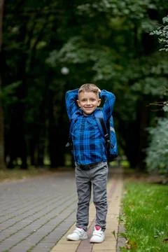 Boy of school age with a blue backpack goes to school in the park Stock Photos