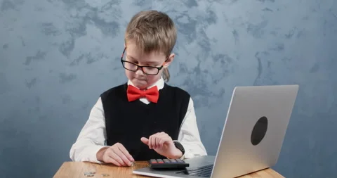 Boy in school uniform calculates stack of coins near computer 動画素材 304367507