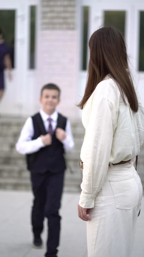 A boy in school uniform comes down the stairs toward his mother.  Stock Footage 344312665