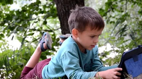 Boy schoolboy with a tablet in a lake plays games, watches cartoons Stock Footage 131237560