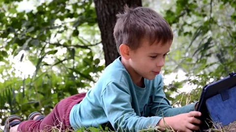 Boy schoolboy with a tablet in a lake plays games, watches cartoons 库存影片 131237571