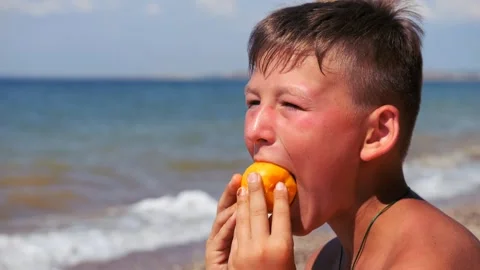 A boy by the sea eats a peach. A light breeze blows over a person. Waves on the Stock-Footage 311407142