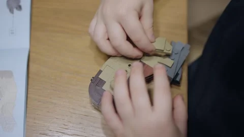 Boy seated at table assembles toy construction set following to instruction Stock Footage 268341122