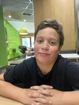 A boy is seated at a table with his hands clasped. He is in a well-lit indoor Stock Photos