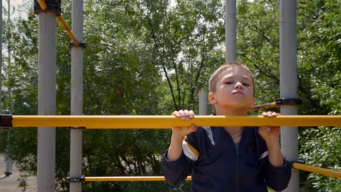 A boy is seen pulling himself up on a horizontal bar on a sunny day. Stock Footage 295814872