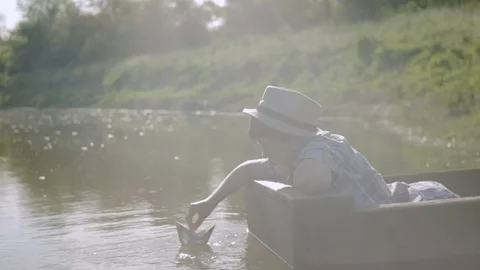 Boy sends sailing ship from the newspaper while sitting in a boat Stockbeeldmateriaal 76182191