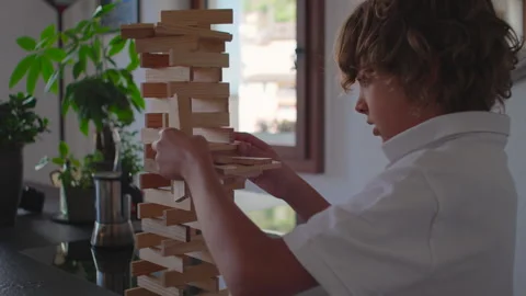 Boy shaping complex tall wooden tower with slow deliberate precision while placi Stock Footage 323702023