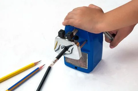 A boy is sharpening his pencil using mechanical sharpener over white backgrou Stock Photos